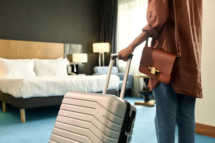 Cropped back view of woman entering hotel room and holding suitcase