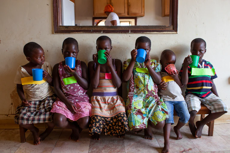 Children sitting on a bench, drinking from mugs