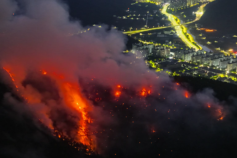 Fire on a hillside at night with city lights in the distance.