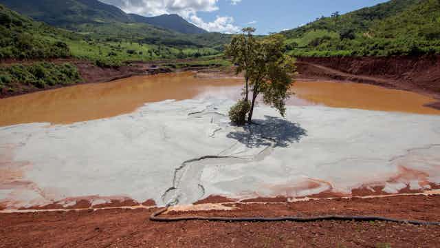 A giant pond of about 800 metres across holding brown sludge with tiny walls - this is a mine tailings dam