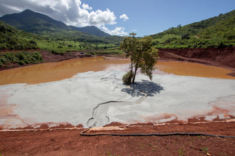 A giant pond of about 800 metres across holding brown sludge with tiny walls - this is a mine tailings dam