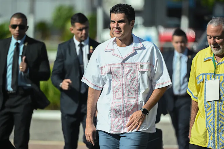 Um homem de mangas curtas caminha com um grupo atrás dele.