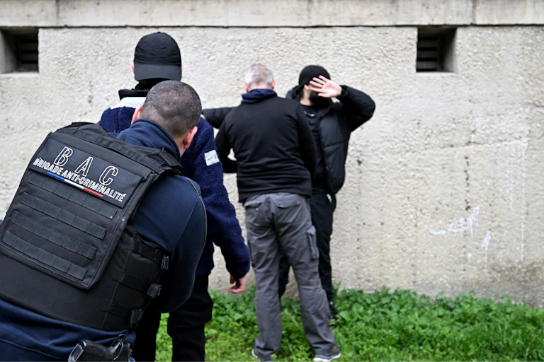 Des policiers de la brigade anti-criminalité (BAC) contrôlent des jeunes hommes devant un bâtiment utilisé par des trafiquants de drogue dans un quartier d'Avignon, dans le sud de la France, le 13 mars 2025. Alors que l'Assemblée nationale examinera à partir du 17 mars 2025 la proposition de loi « visant à sortir la France du piège du trafic de stupéfiants », Avignon - comme Grenoble ou Rennes - est un exemple de ces villes moyennes rattrapées par le fléau.