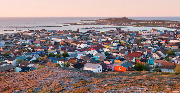 A fishing village of brightly coloured houses at sunrise with the ocean in the background.