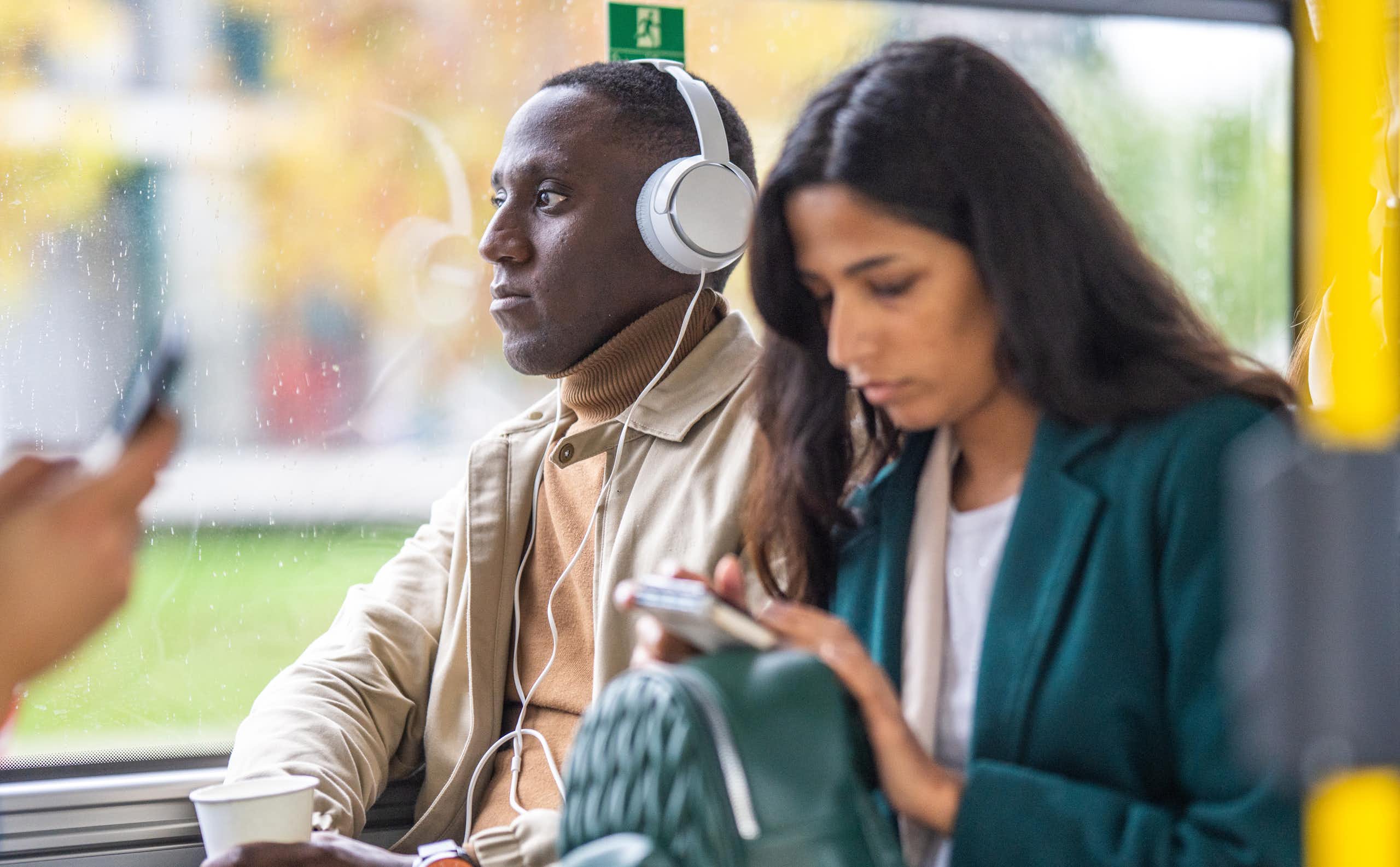 man in headphones next to woman looking at phone, in their own worlds