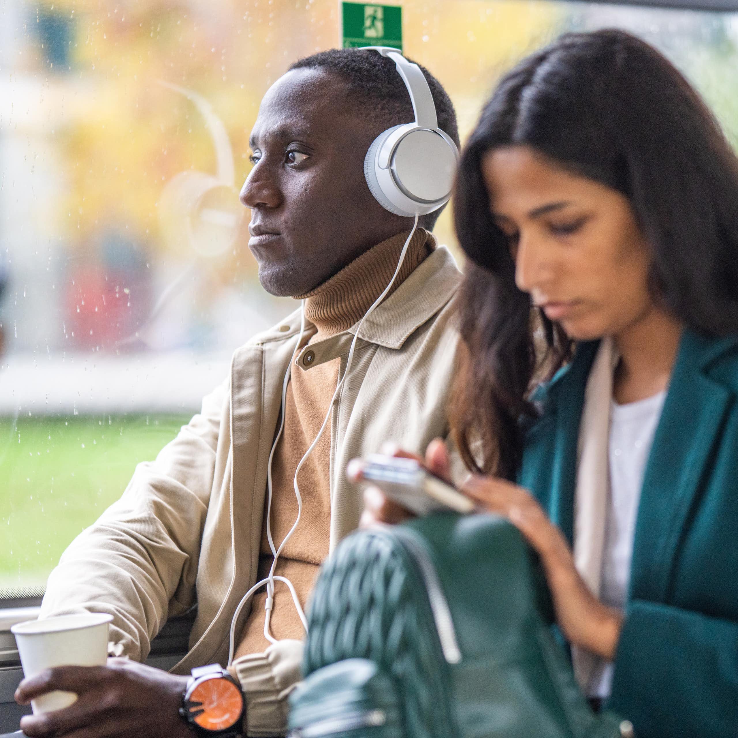 man in headphones next to woman looking at phone, in their own worlds
