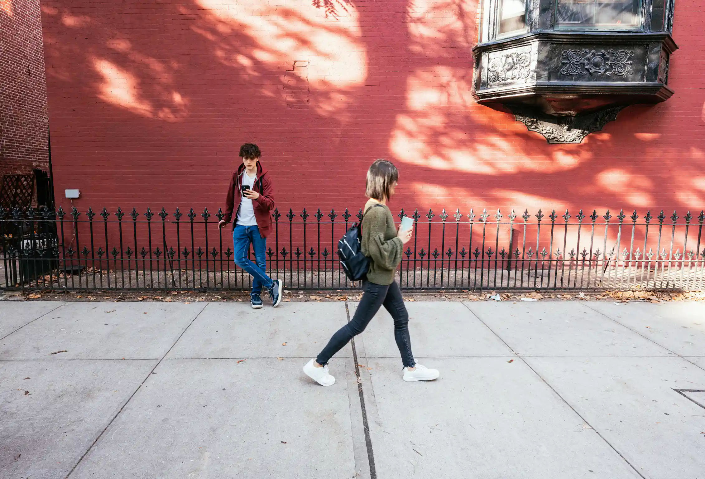 young woman walks past a young man who is staring down at his phone