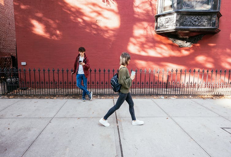 young woman walks past a young man who is staring down at his phone