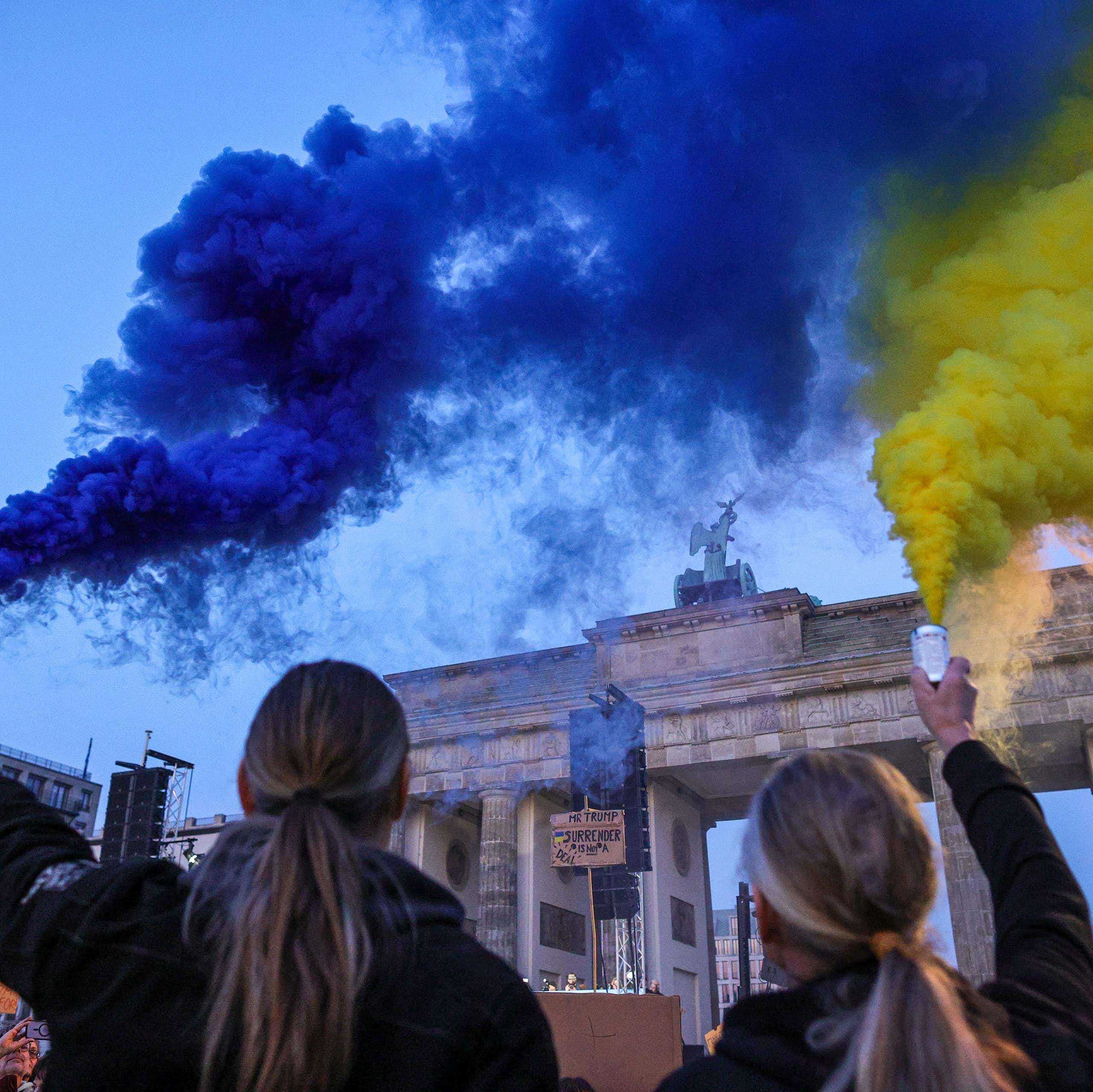 Two people hold flares: one emiting blue smoke, the other yellow.
