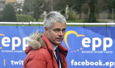 A man with short grey hair in an orange parka with fur-trimmed hood.