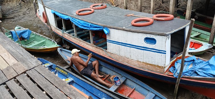foto mostra pequenas embarcações na beira do rio. Um pescador está deitado numa canoa