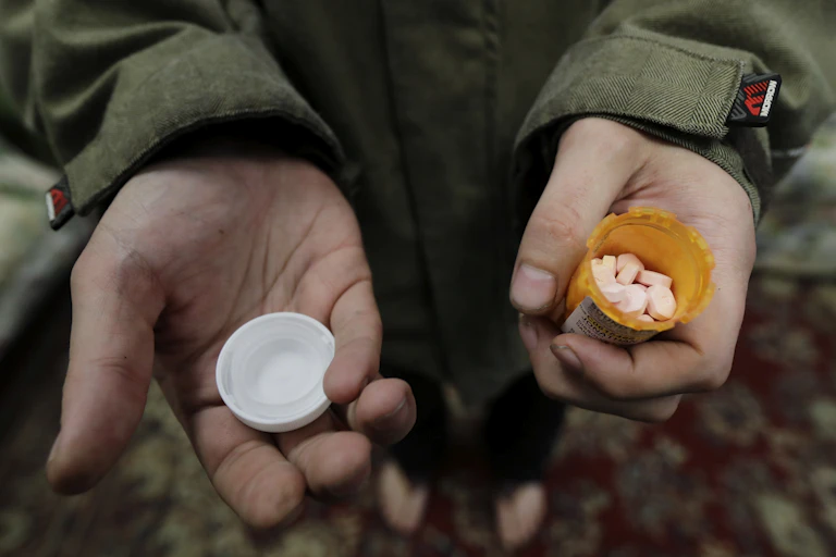 Close-up of person's hands holding an open bottle of white pills
