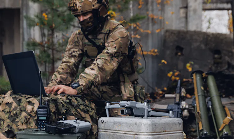 A soldier in fatigues and a face mask working at a lap top