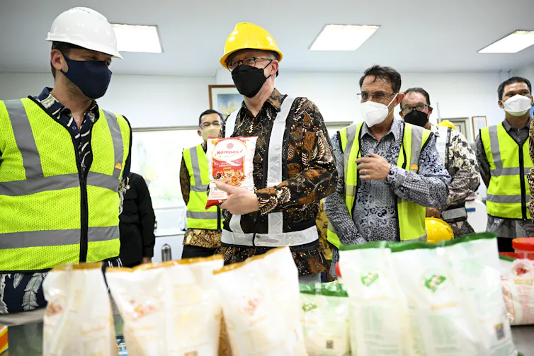 Wearing safety gear and a printed shirt, Albanese poses for cameras with a bag of flour.
