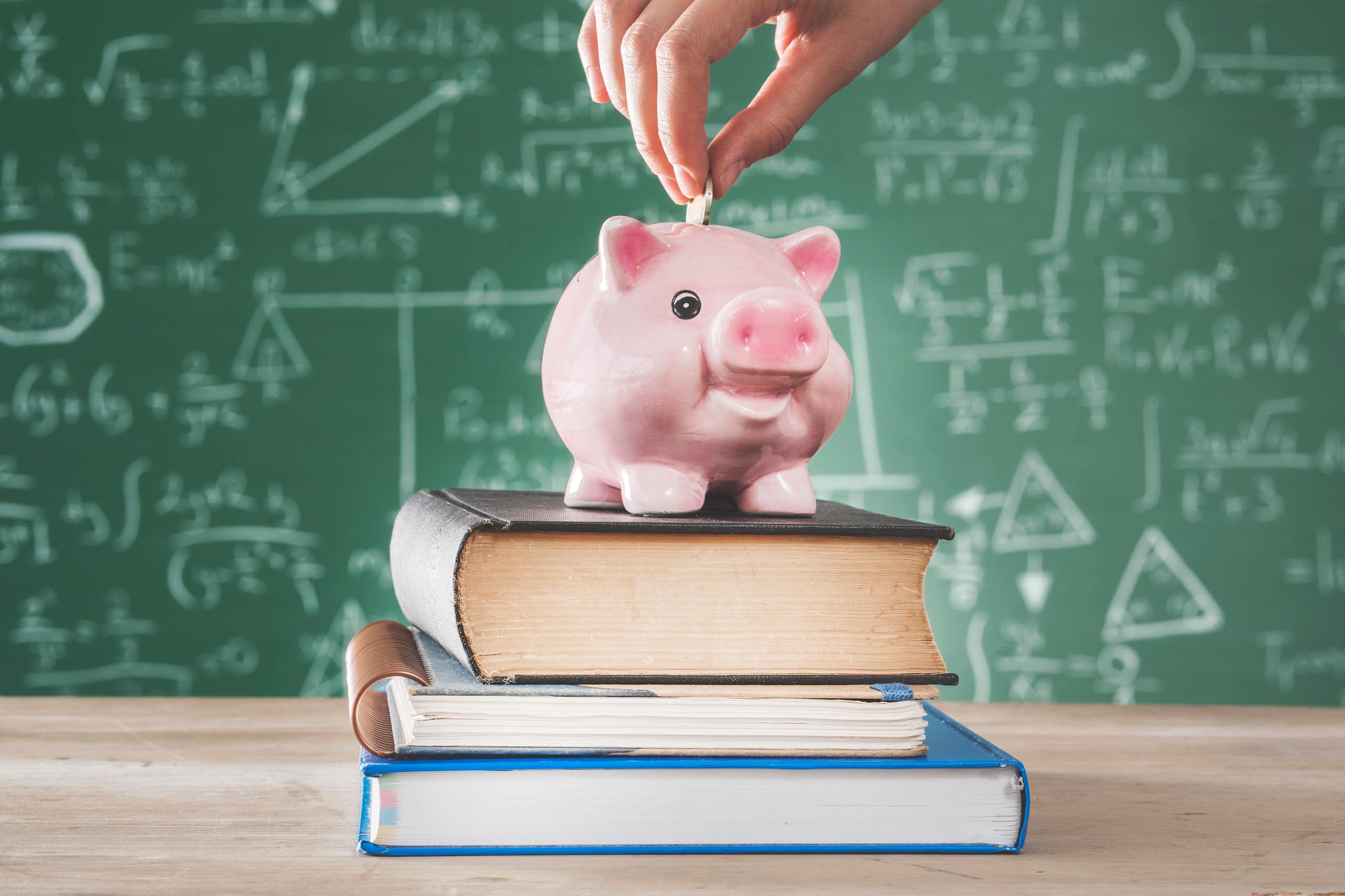 Female putting coin into piggy bank on a stack of text books in front of a blackboard