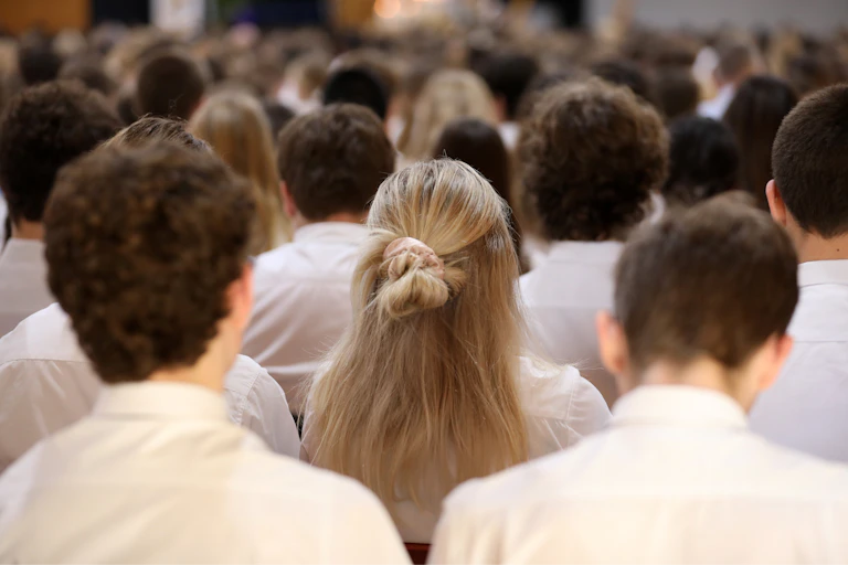 Young people in white shirts sit in rows.