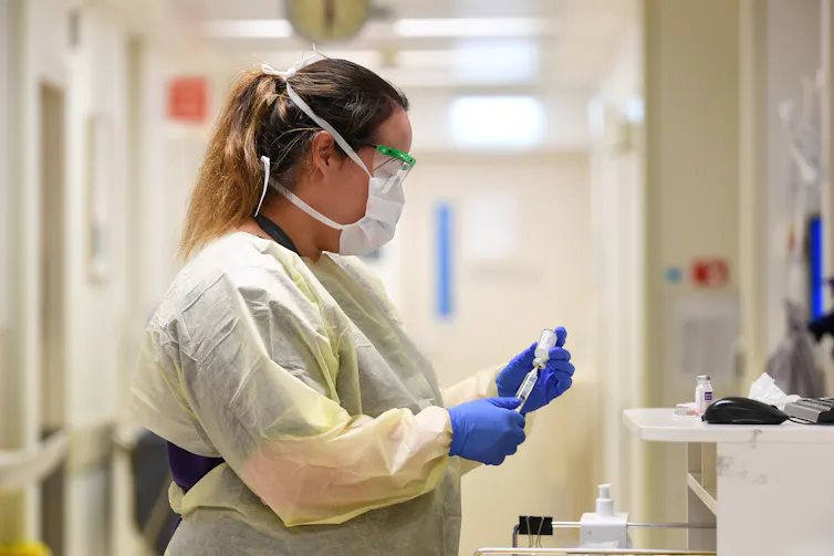 Woman wearing personal protective equipment holding a syringe