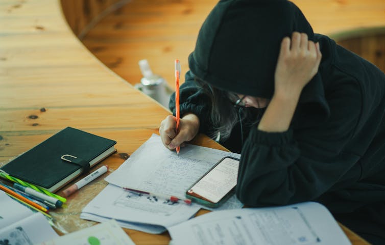 A young person in a hoodie works at a desk.
