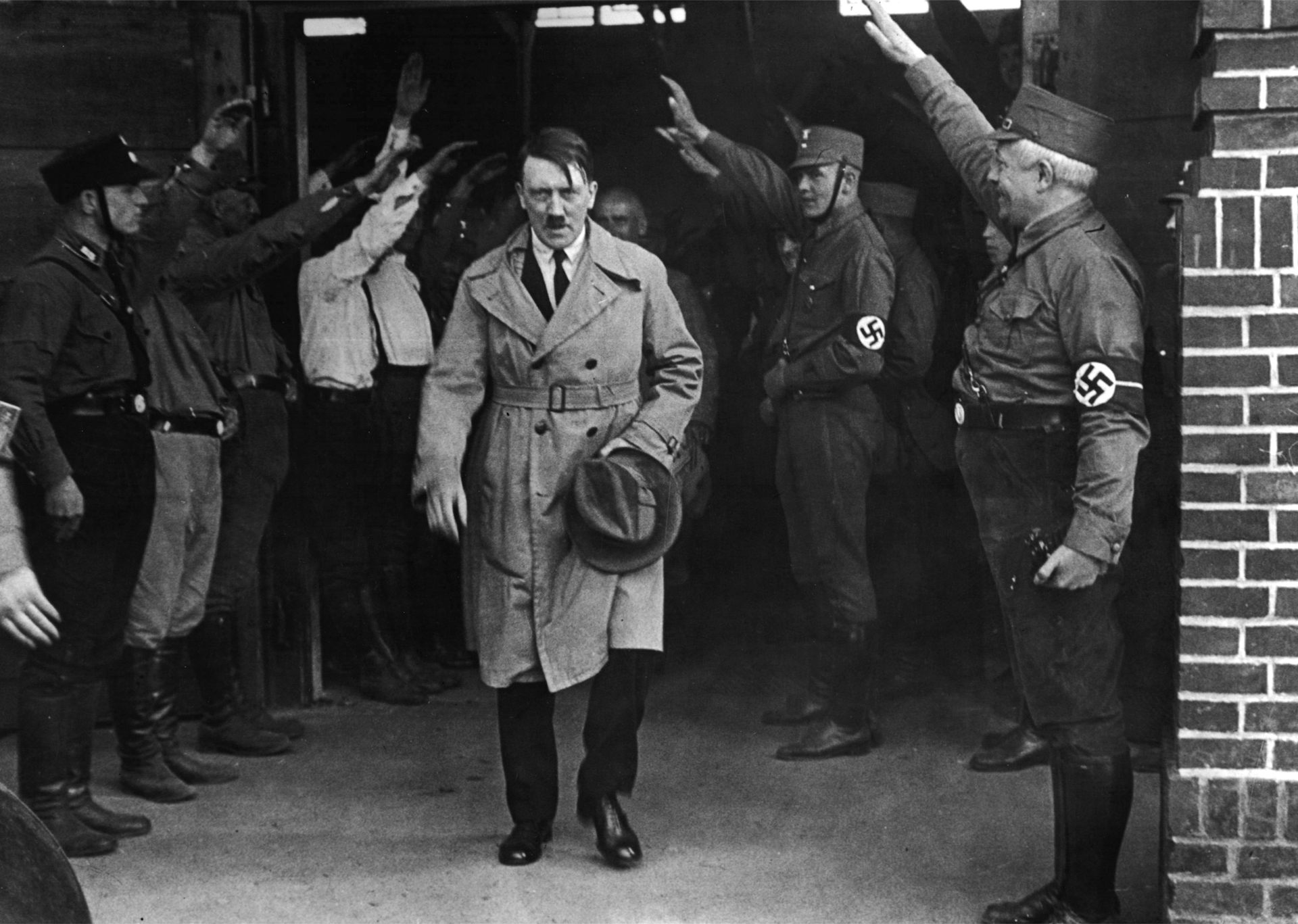 Adolf Hitler emerging from a brick building with Nazis in uniform saluting on either side of him
