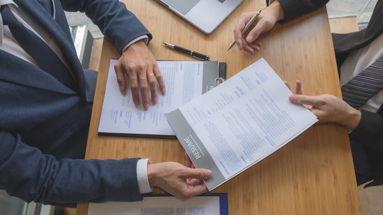 Overhead view of a person in a suit handing another person in a suit a resume