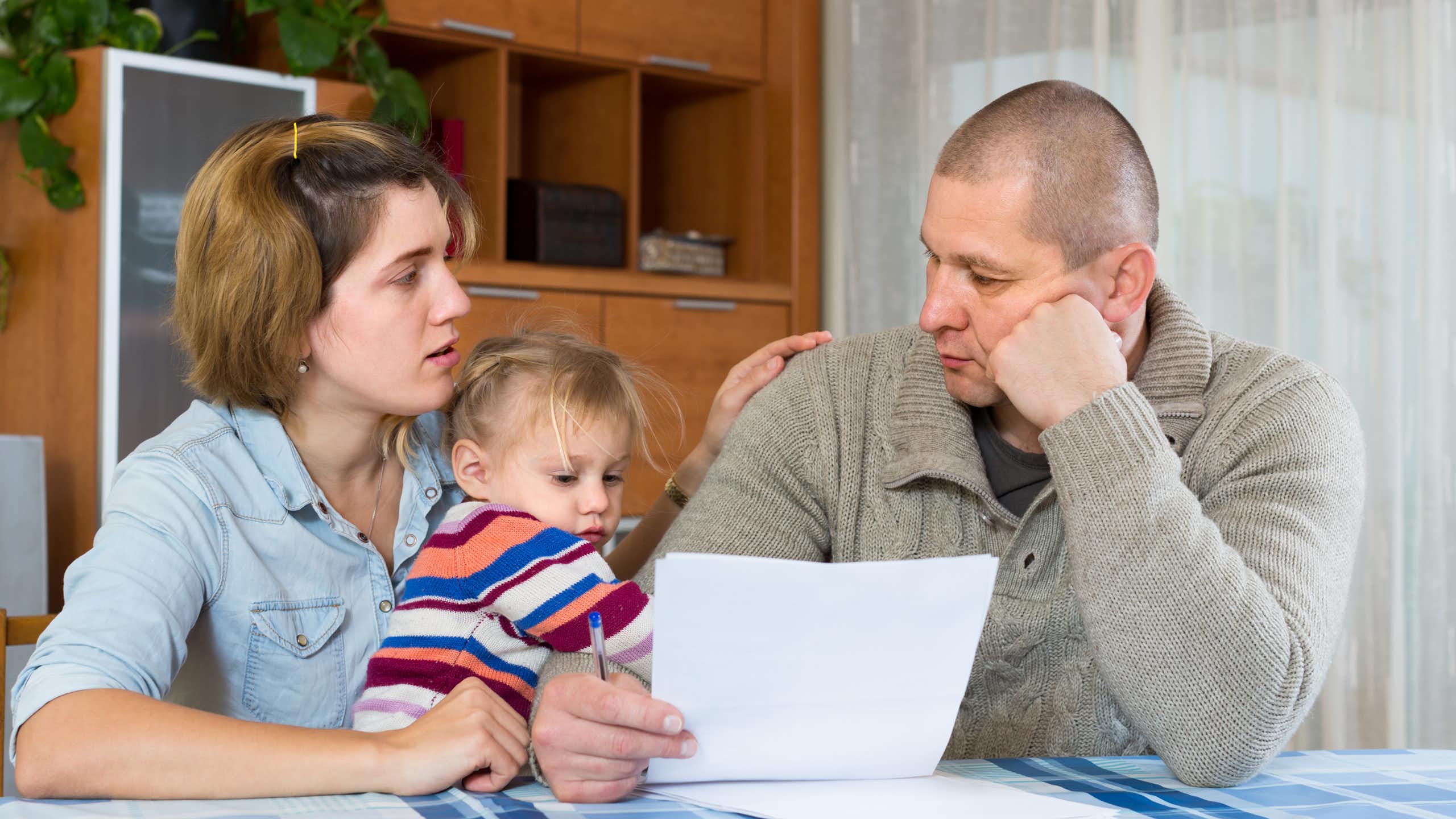 Worried family with child sitting with financial documents at home.