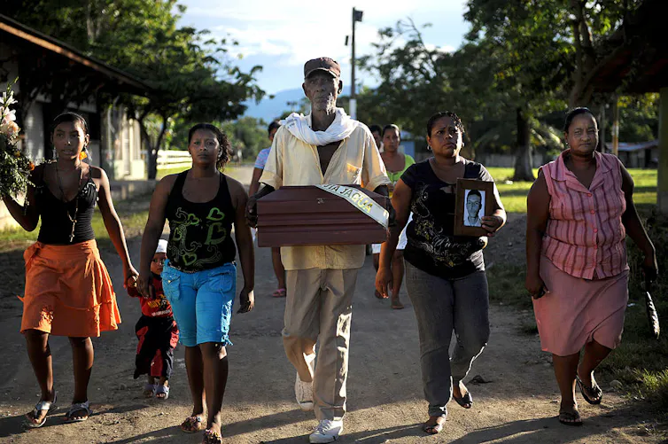 Four women walk down a path as a tall man in a white shirt walks in the middle.