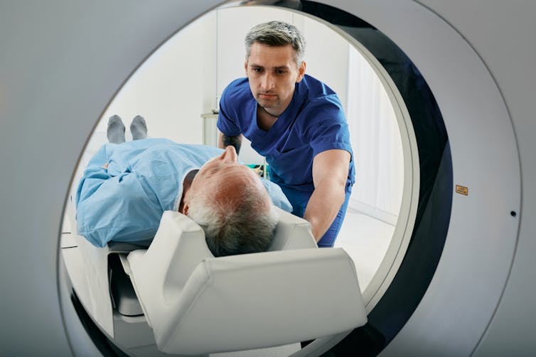 Male health worker pushing man lying down into CT scanner
