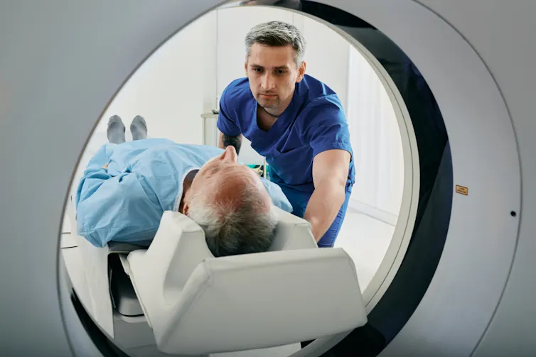 Male health worker pushing man lying down into CT scanner