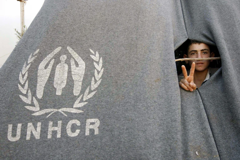 A refugee flashes the piece sign from inside a tent.