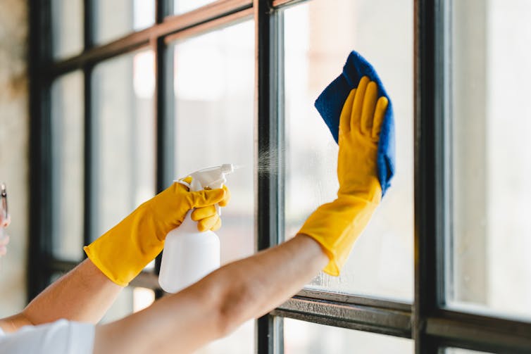 Gloved hands cleaning a window with spray.
