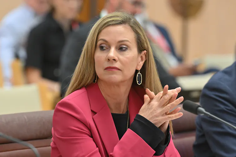 A woman with blonde hair wearing a pink blazer.