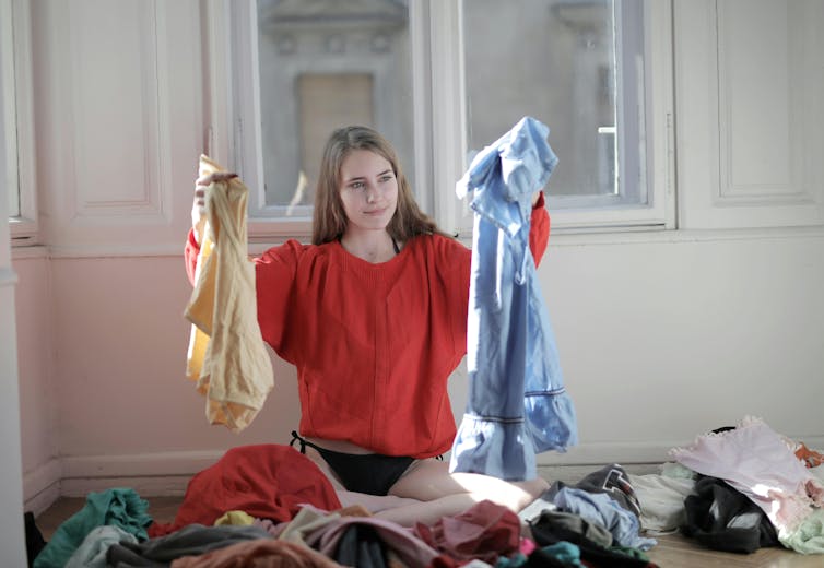 A woman folding laundry with clothes scattered across her bed.
