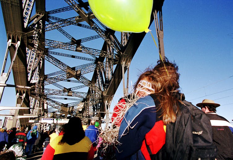 A child holds an balloon and smiles at the camera over their mother's shoulder