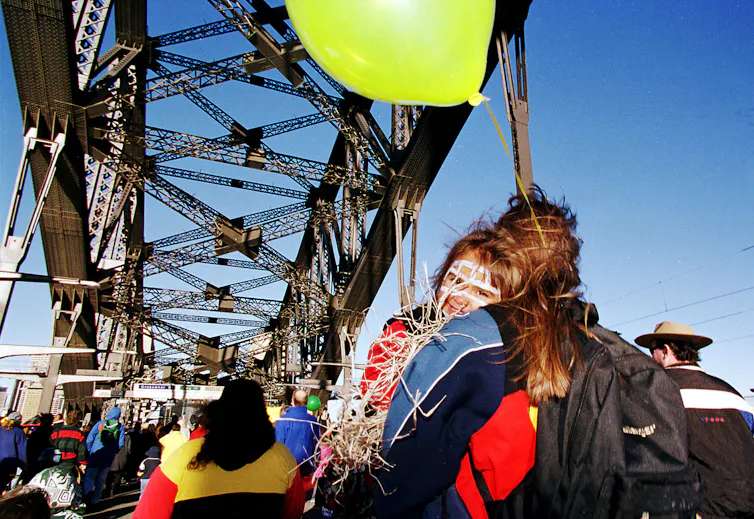 A child holds an balloon and smiles at the camera over their mother's shoulder