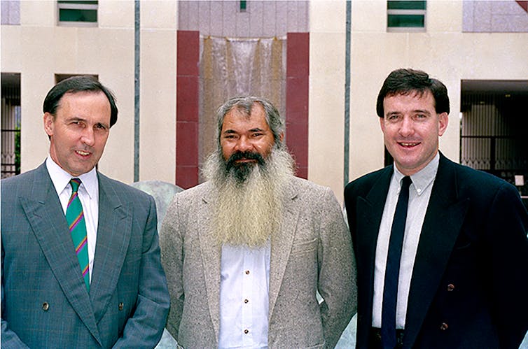 Three men stand next to each other and smile in parliament house
