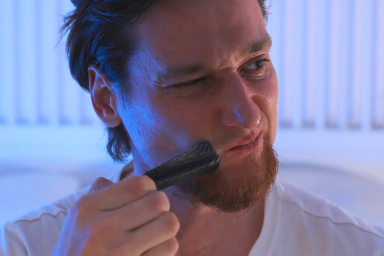 A man in bed pulling black tape off his face and wincing.