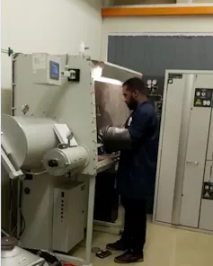 A man stands in front of a giant machine taller than his head with his hands inside a silver tube