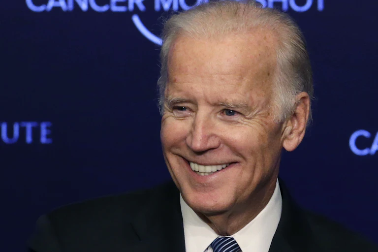 Joe Biden smiling in front of a backdrop reading 'CANCER MOONSHOT'