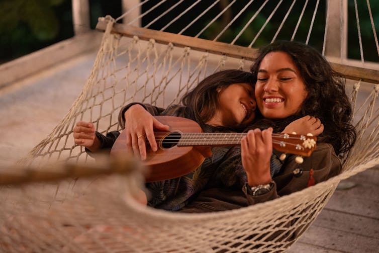 A pretty woman with a child playing guitar lying on a hammock.