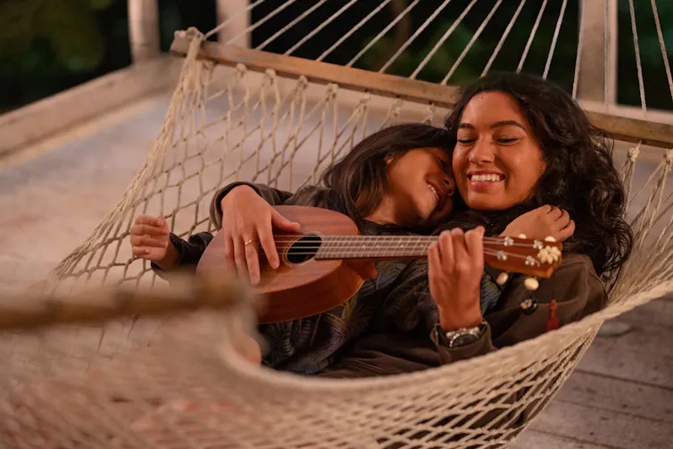 A pretty woman with a child playing guitar lying on a hammock.