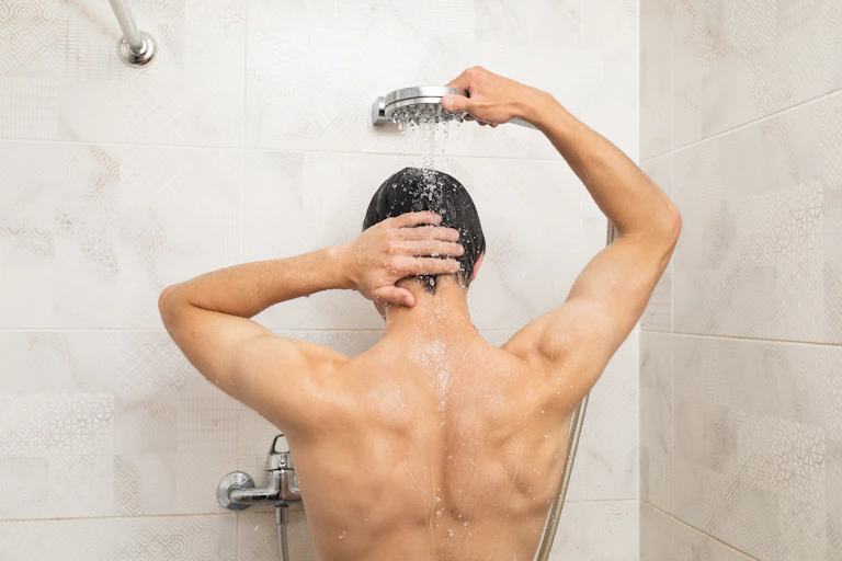 Un homme utilise une pomme de douche pour se rincer les cheveux sous la douche.