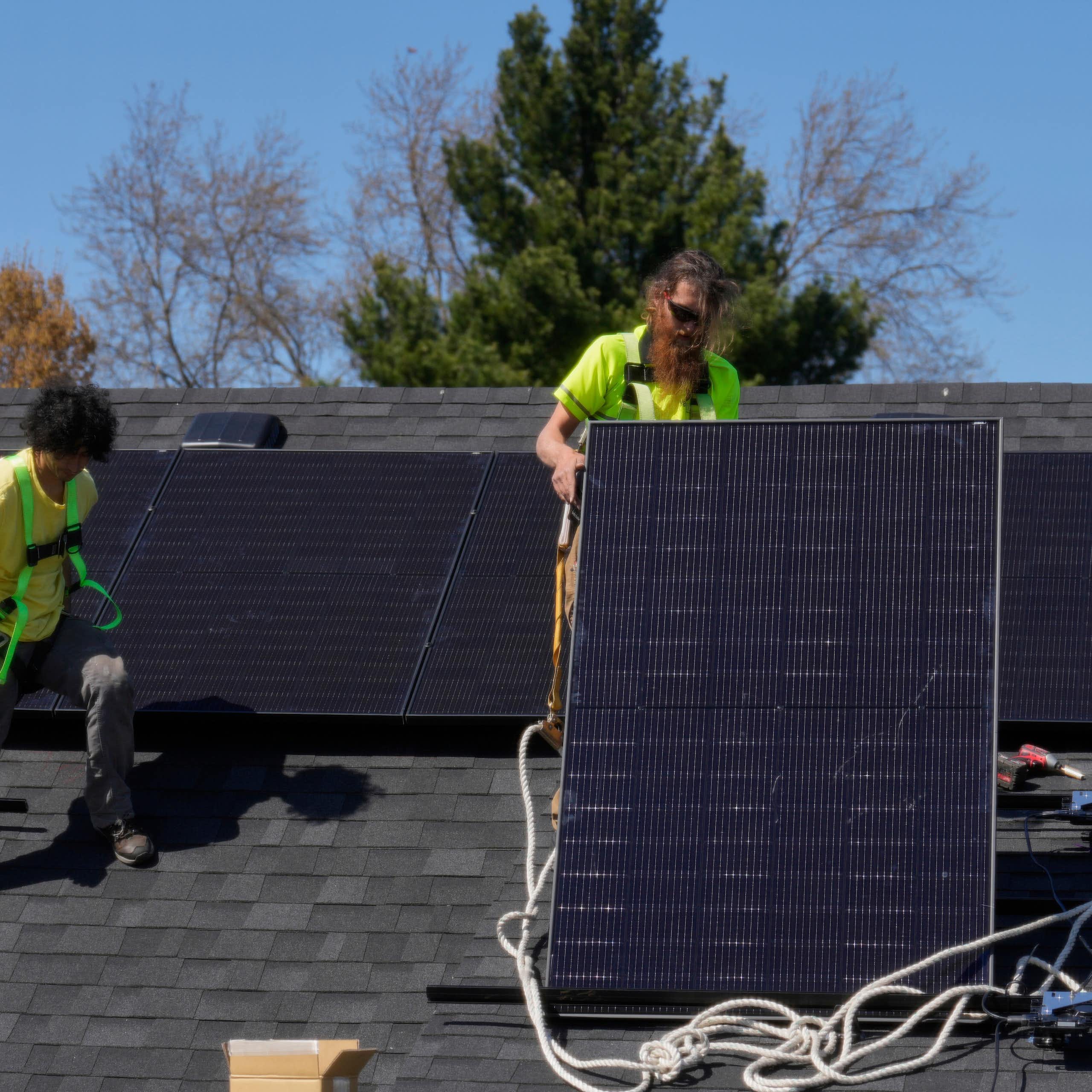 Two people move solar panels around on a rooftop.