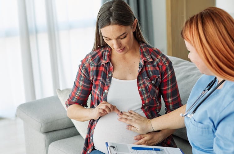 A young woman in a white T-shirt and plaid shirt and a nurse in scrubs holding a clipboard