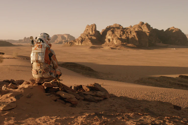 'The Martian' protagonist Mark Watney, donning a space suit, overlooks a Mars-scape.