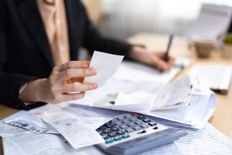 chest of someone seated at desk with calculator and a lot of receipts
