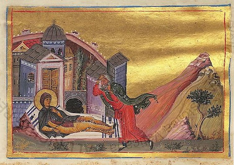 A person lying on a bed appears to be getting up as a man in a long red cloak walks toward him.