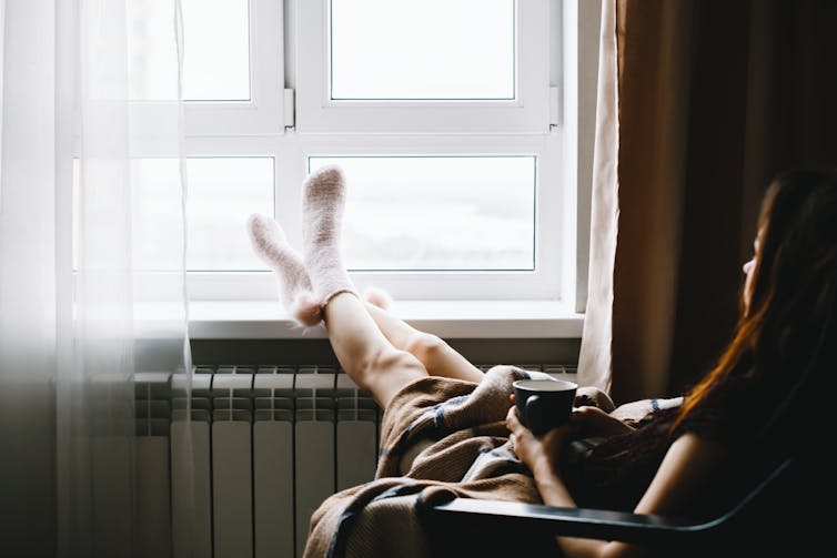 Woman resting feet on heater by window.