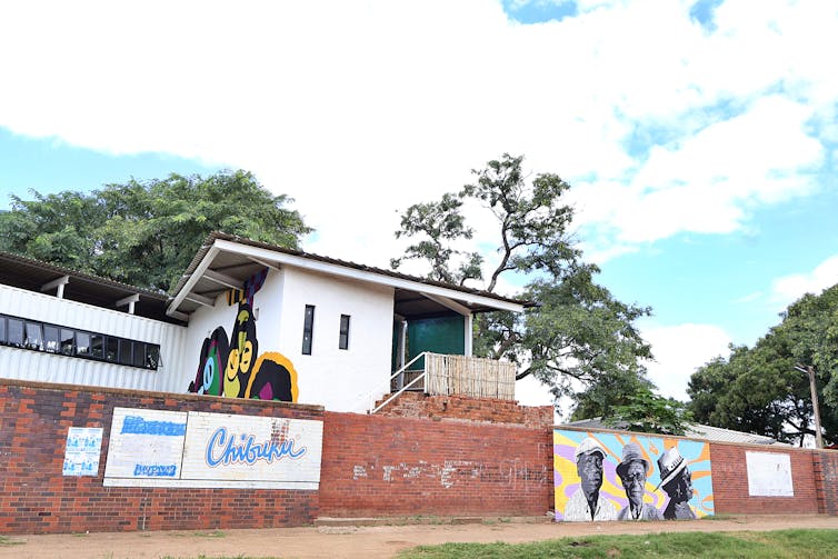 A high brick wall has a colourful mural and signage, behind it a modern white structure.
