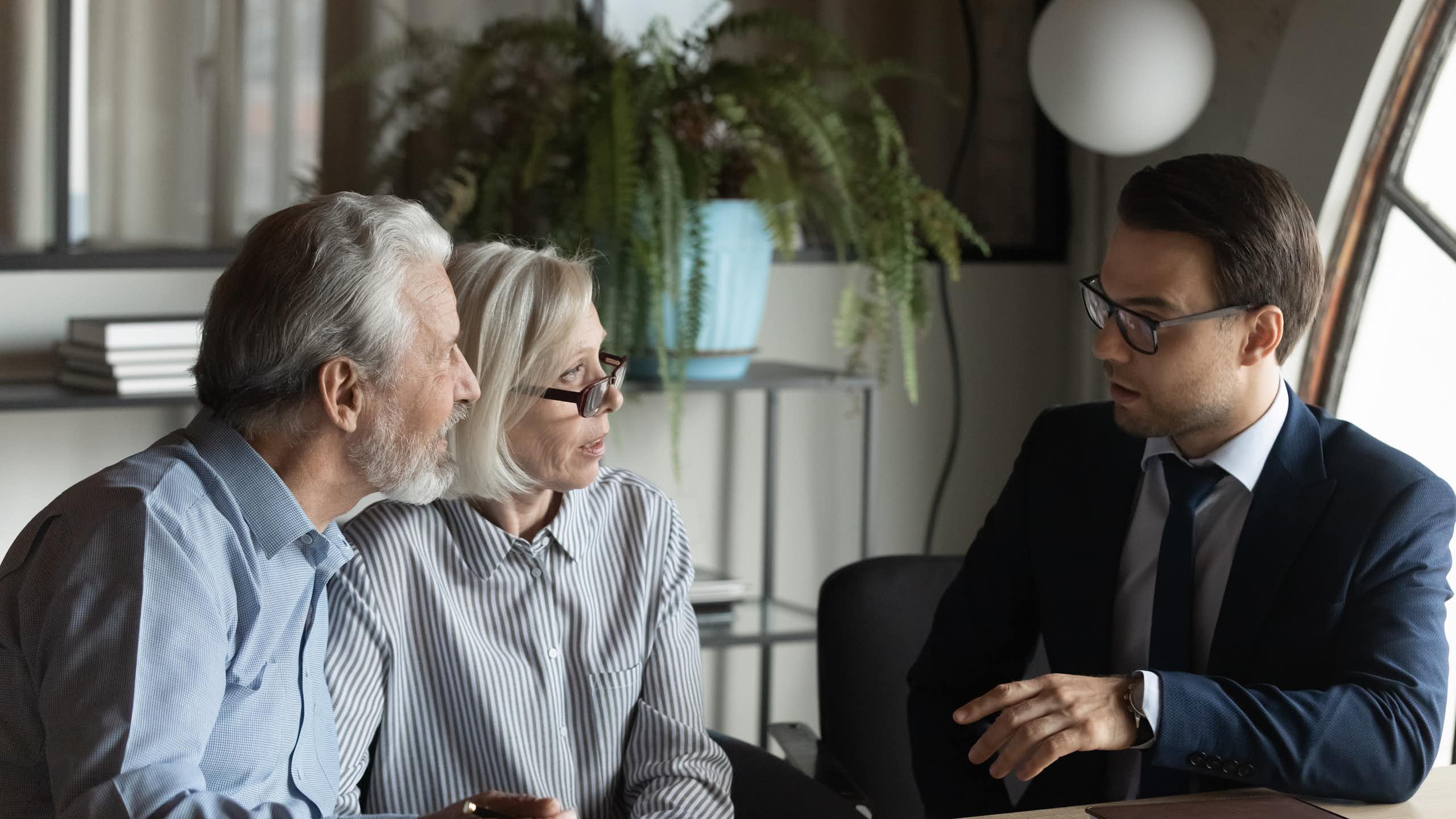 Deux personnes plutôt âgées discutent avec un homme en costume. ils vont peut être signer un contrat