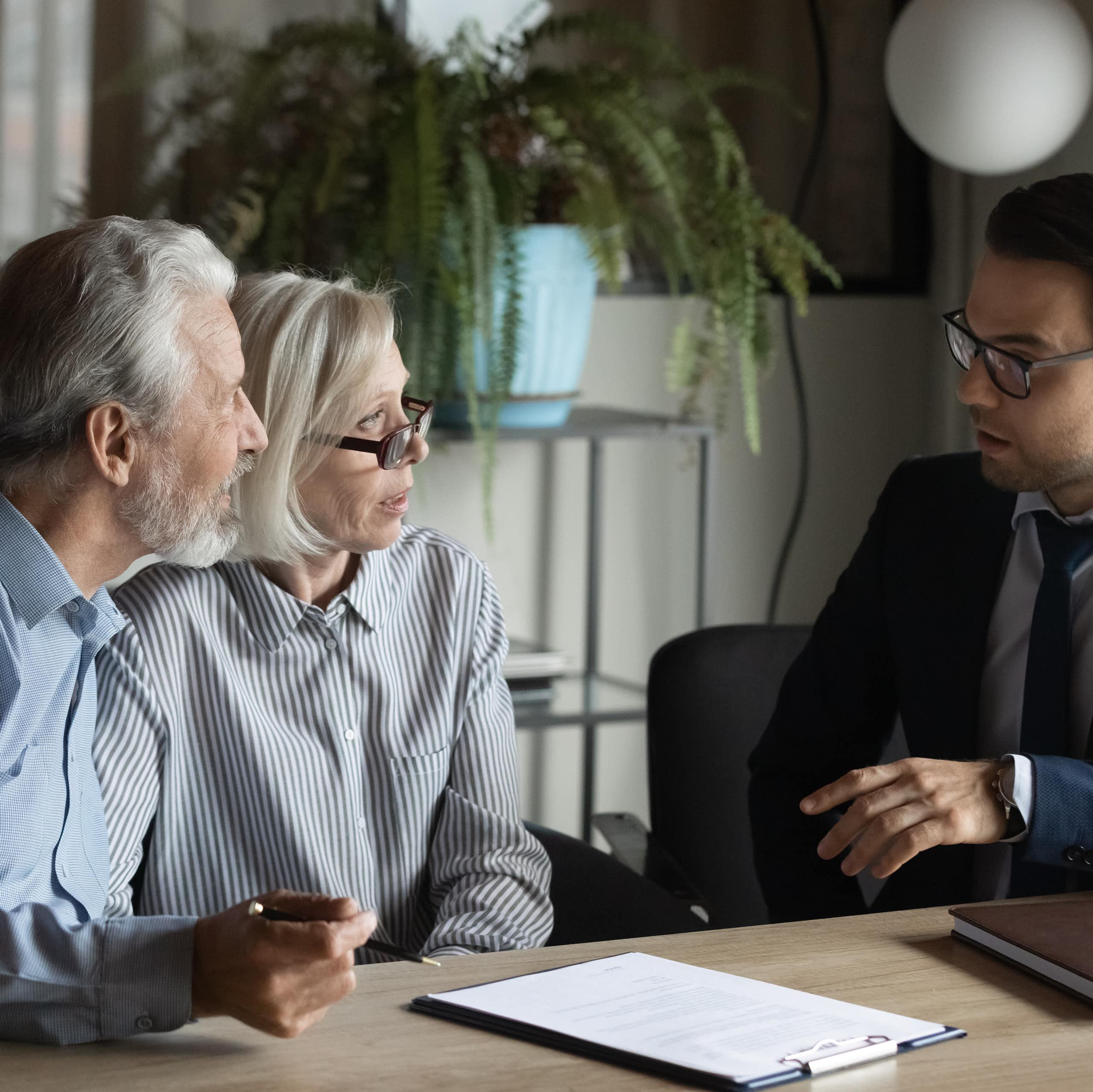 Deux personnes plutôt âgées discutent avec un homme en costume. ils vont peut être signer un contrat